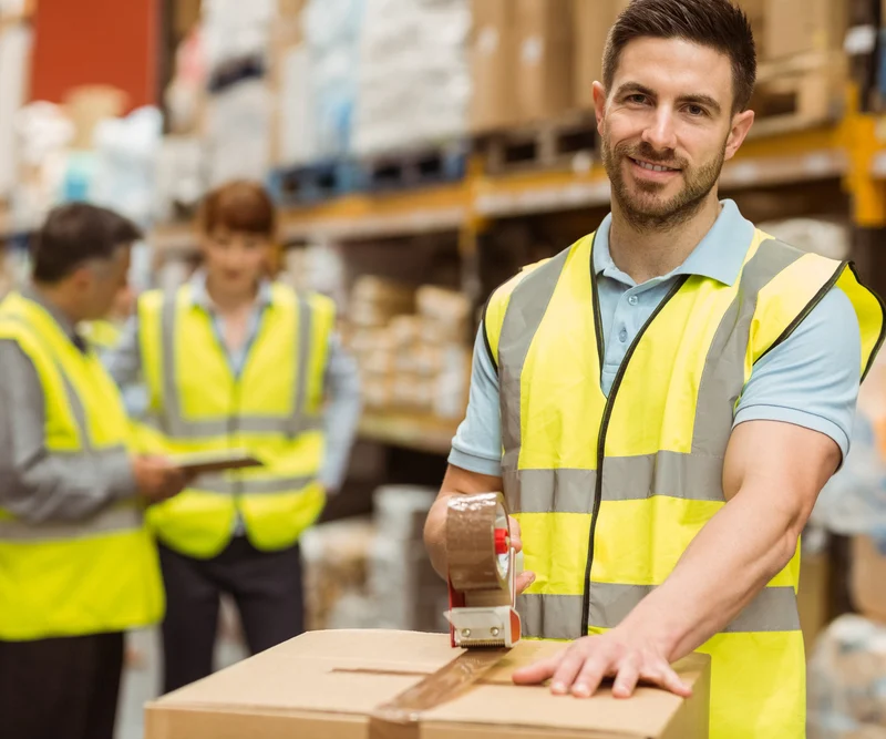 Smiling warehouse workers preparing a shipment in a large warehouse